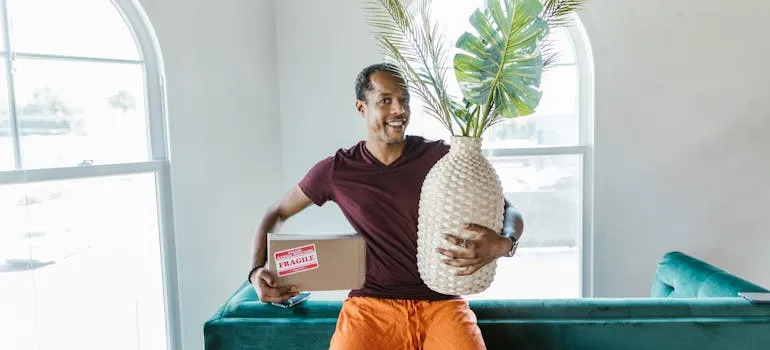 Man holding a box and giant ceramic pineapple indoors near a window